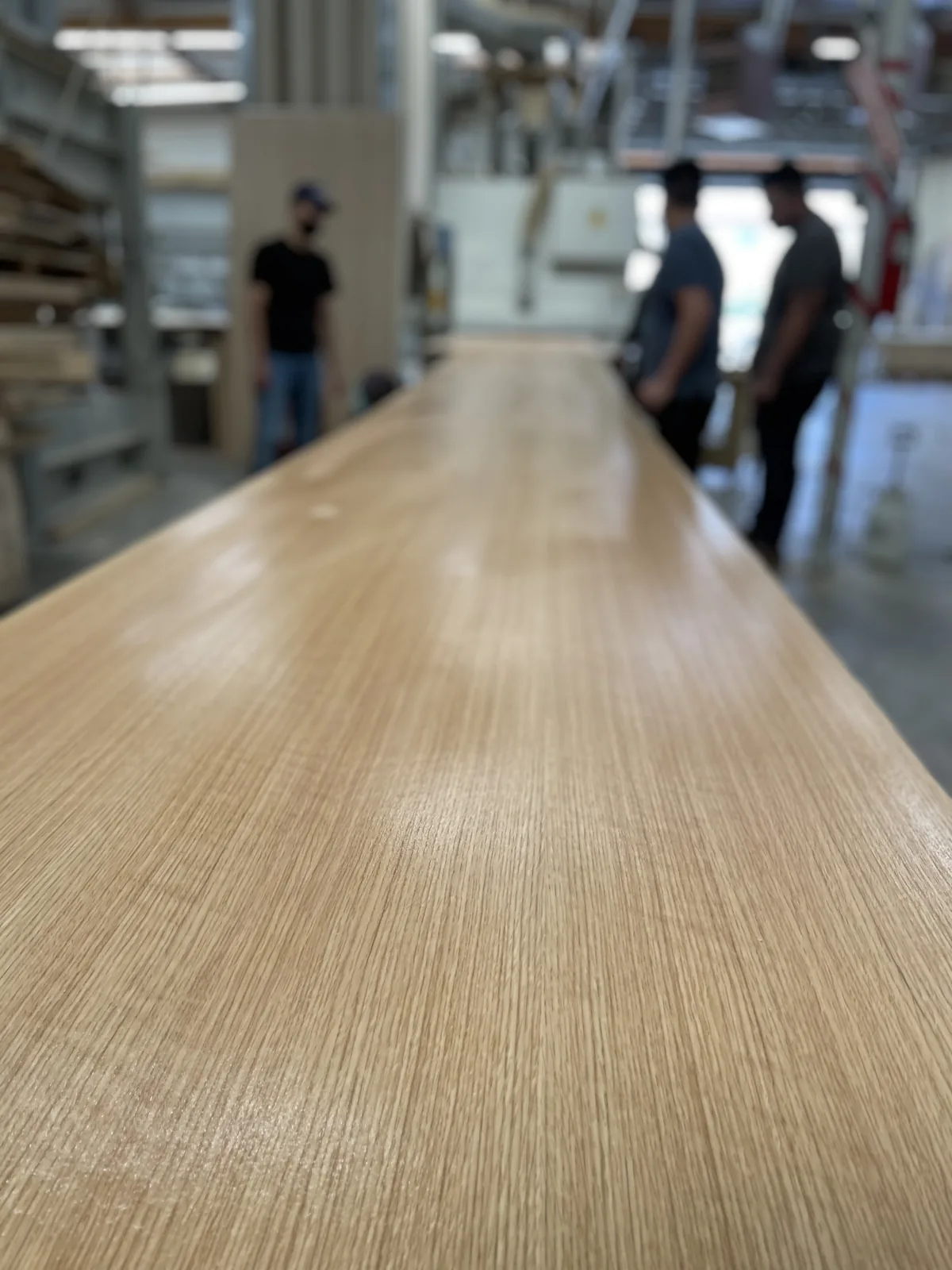 A long veneered panel on the bench, three shop hands at its far end.