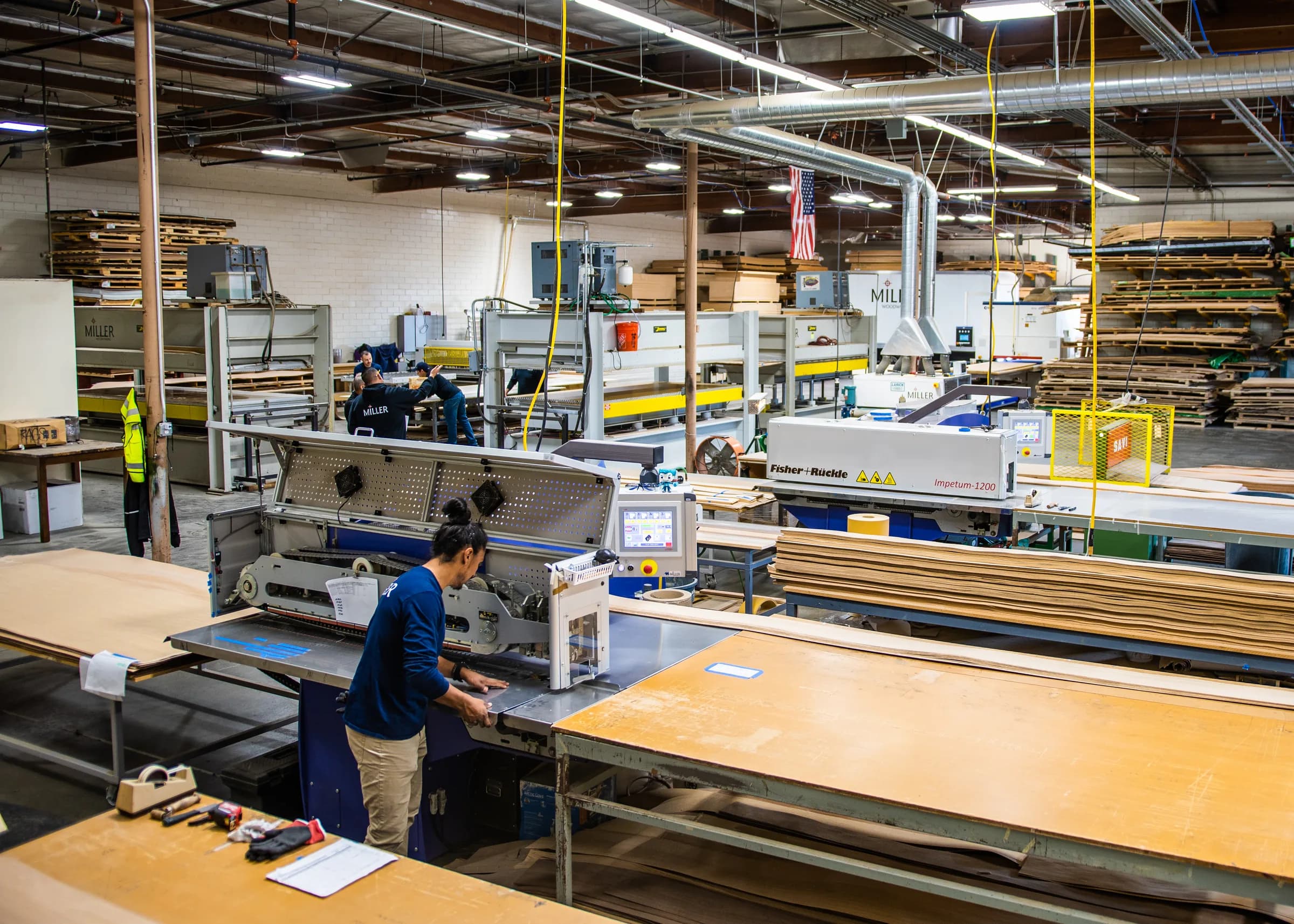 The veneer floor from above: a shop hand at the clipper, the benches and the press beyond.