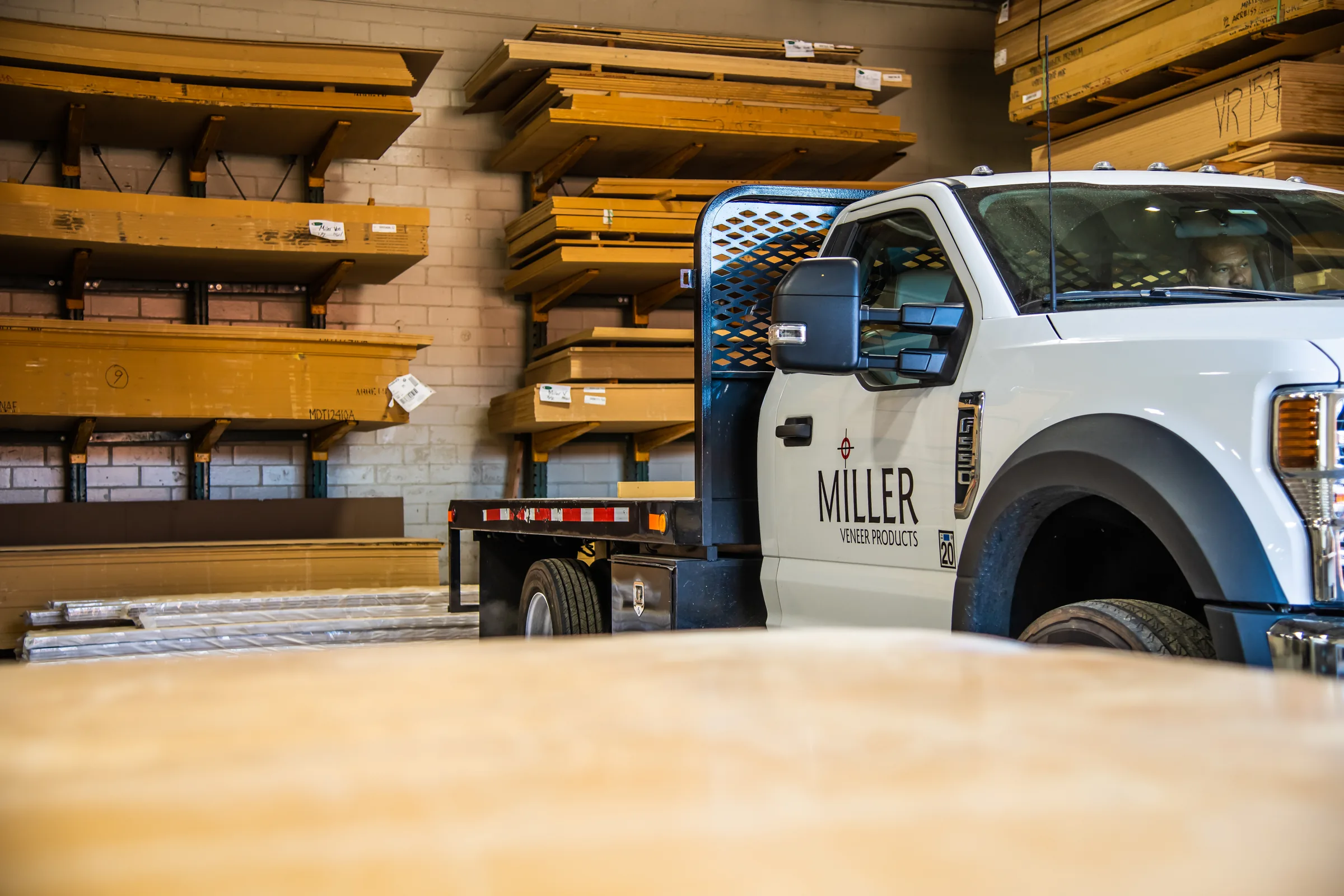 The Miller Veneer Products flatbed backed in beneath the panel racks, a stacked panel in the foreground.