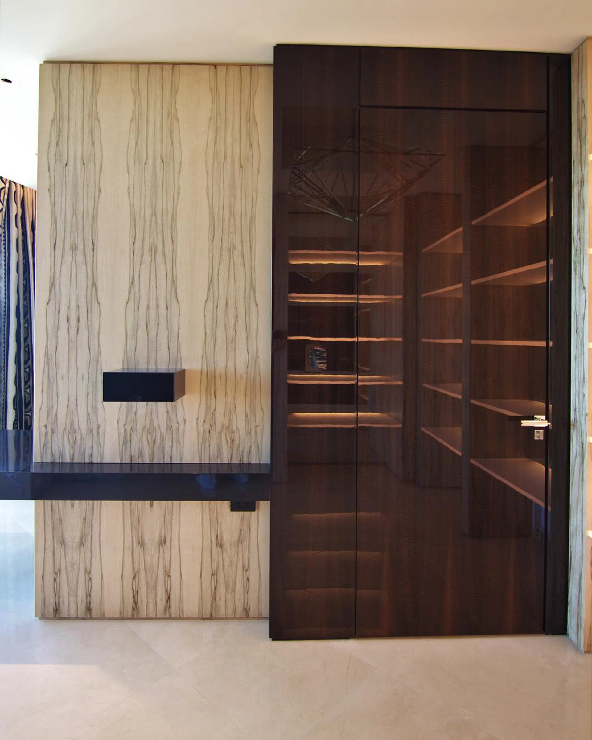 A full-height dark walnut door with fine metal inlay lines, set beside a pale figured oak wall.