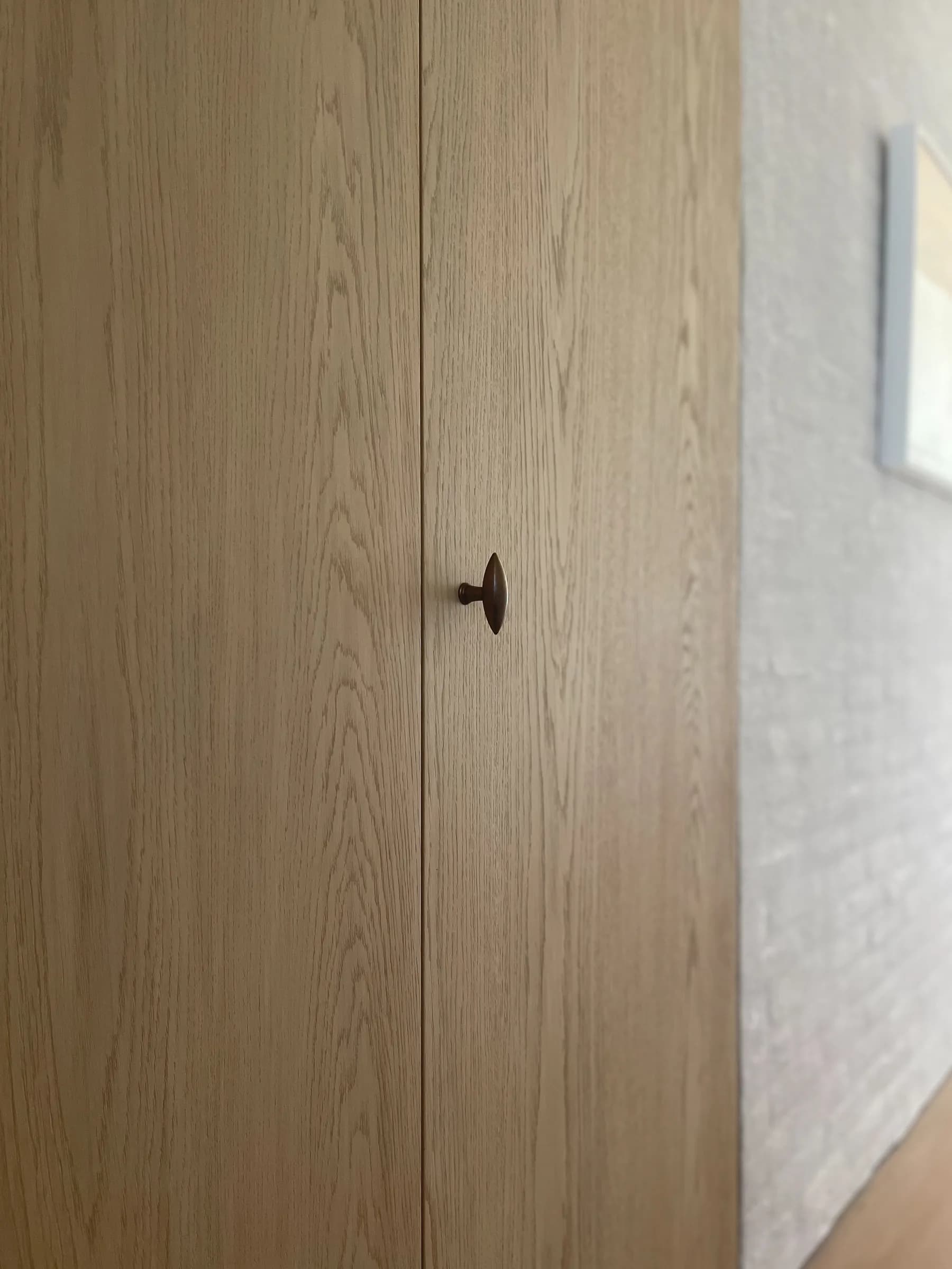 A pale rift oak door with a small dark knob, closed in a plaster wall.