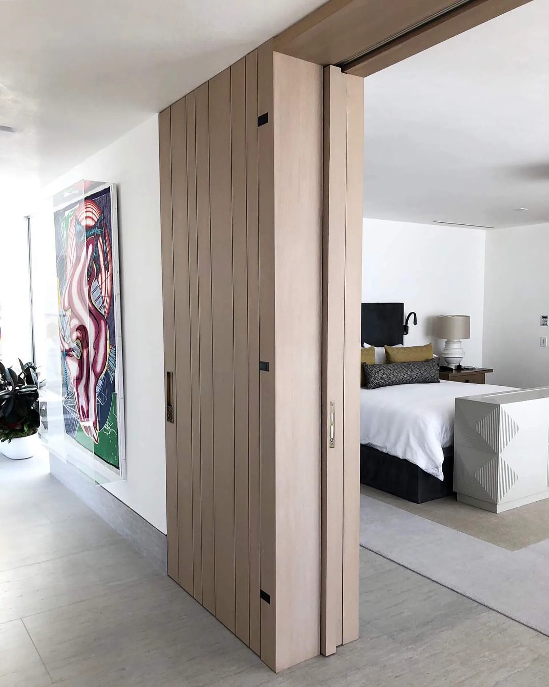 A tall pale oak slab door with vertical grooves, slid open to a bedroom.