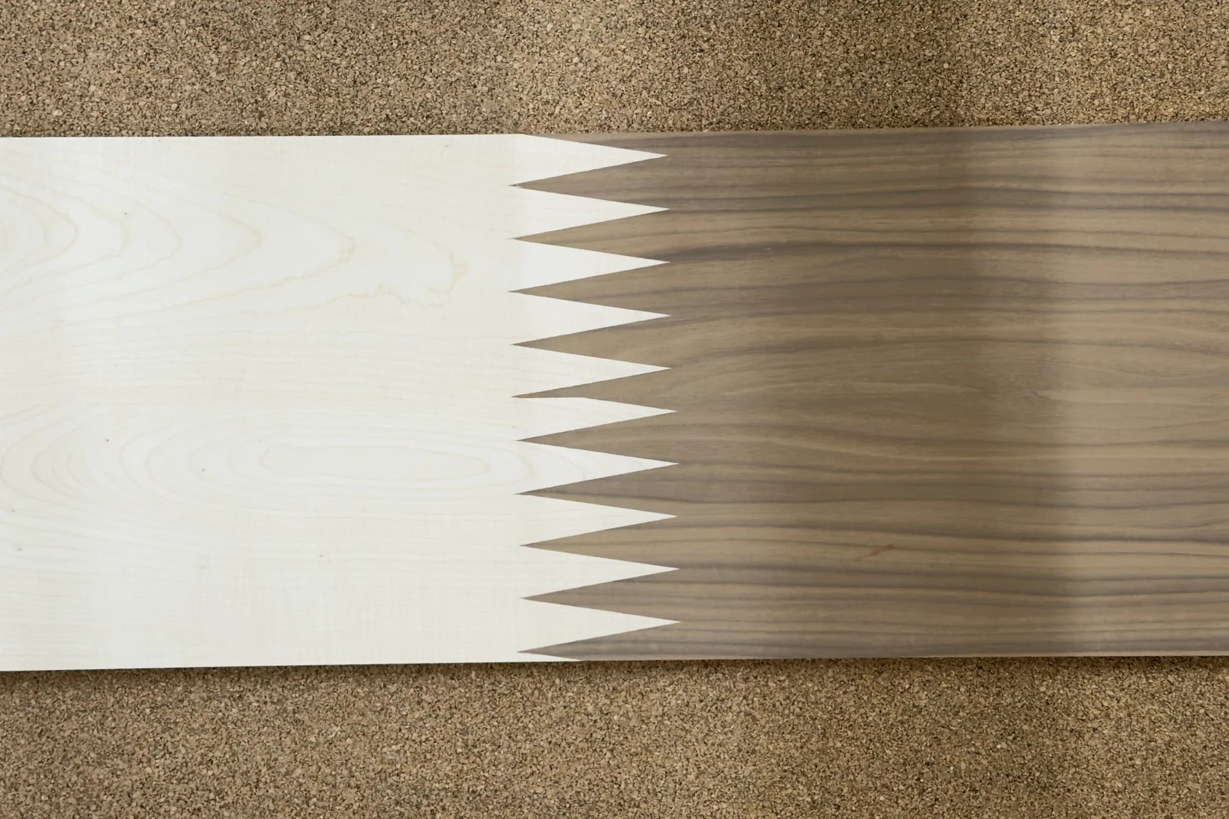 A demonstration panel on the cork bench: figured maple finger-jointed to walnut, the tapered fingers of one species running into the other.