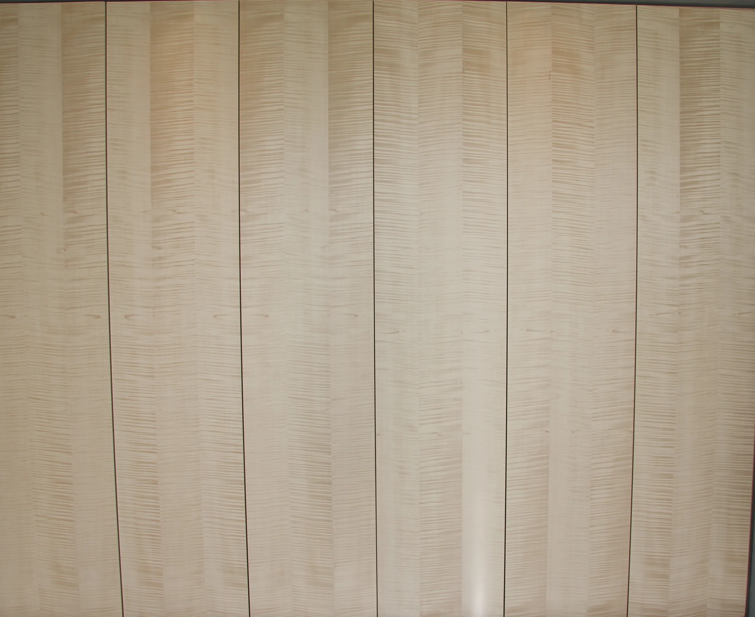 A lit wall of curly-figured veneer panels seen straight on, the leaves meeting edge to edge across every panel.