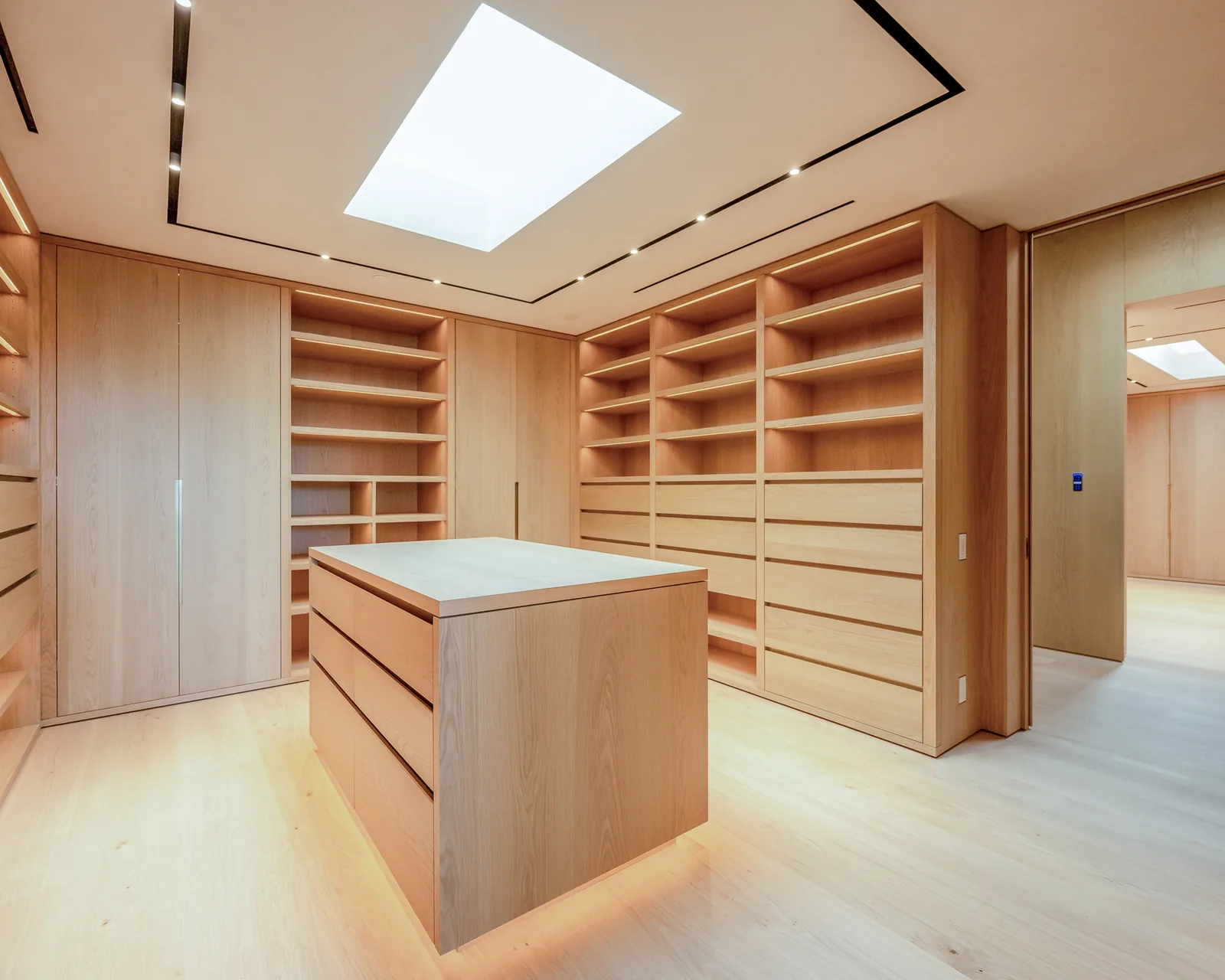 A dressing room in pale veneer, shelving and island built as one continuous grain match.