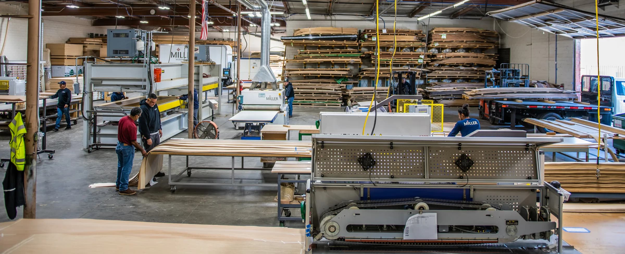 The veneer floor end to end: the seamer in the foreground, shop hands at the benches, the press and the racks beyond.