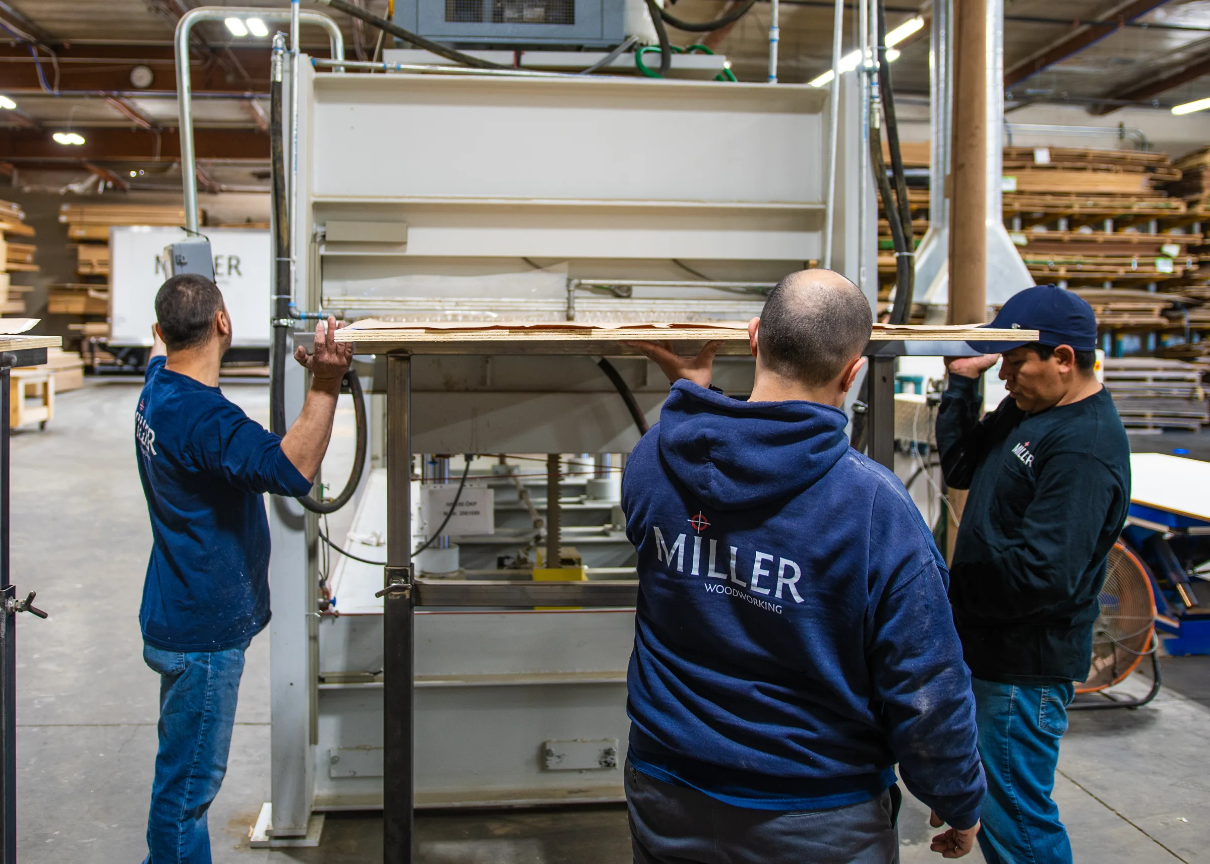 Three shop hands feeding a veneered panel into the press.