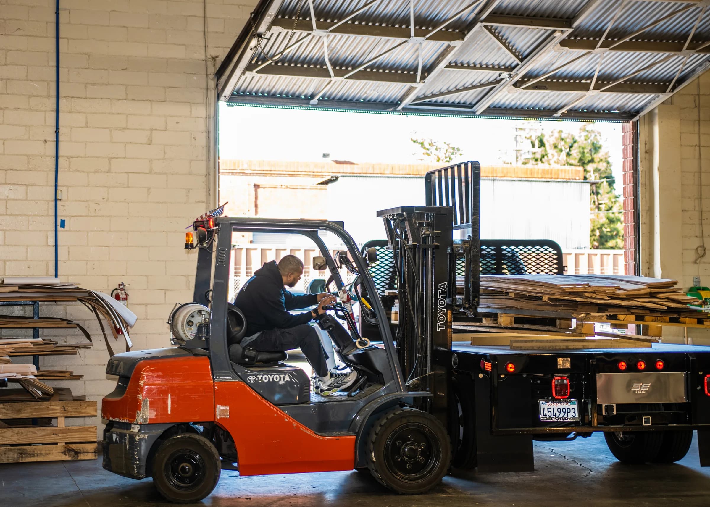 A forklift lifting a stack of wrapped panels onto the flatbed at the open roller door.
