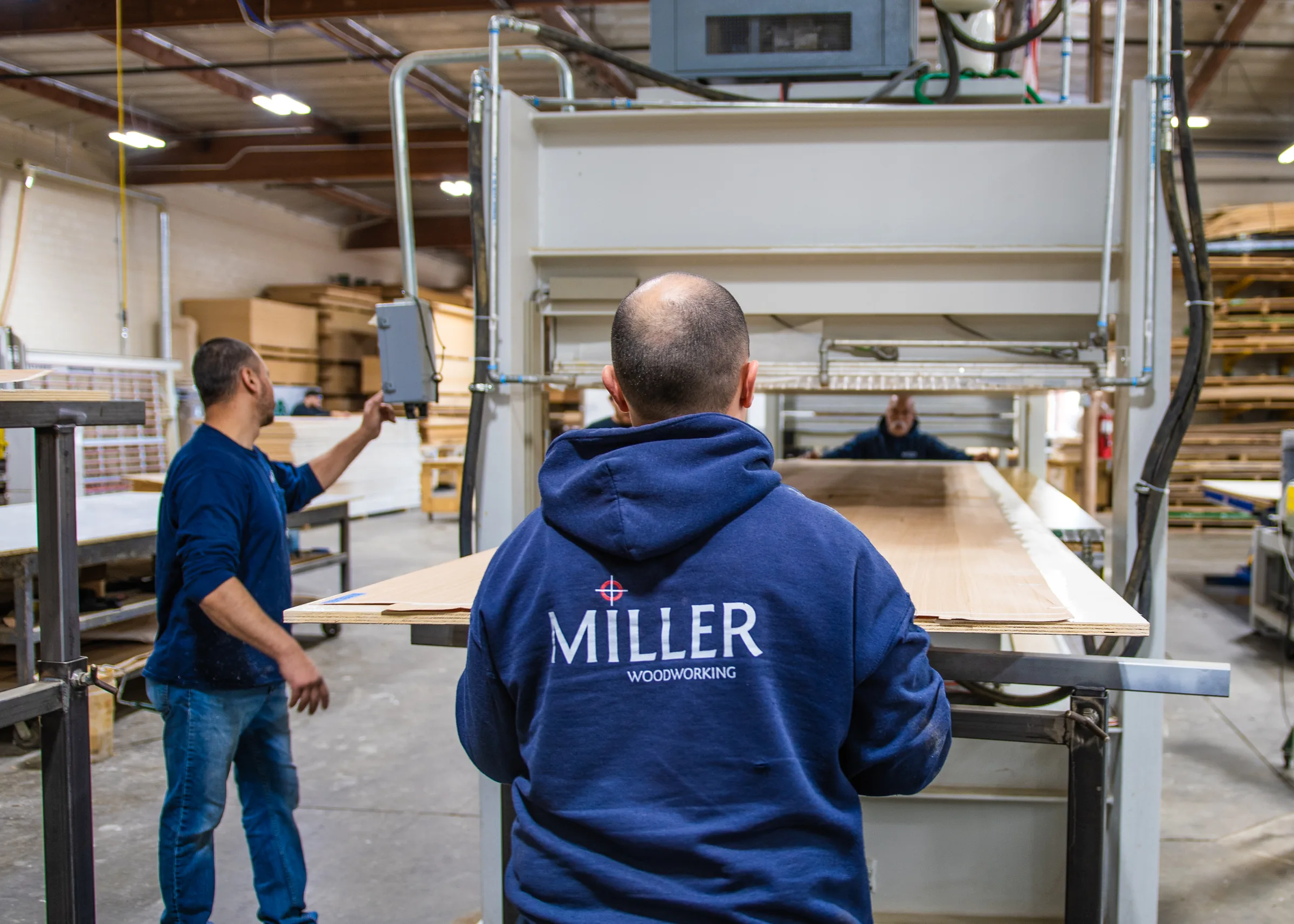 A panel fed into the press by two shop hands.