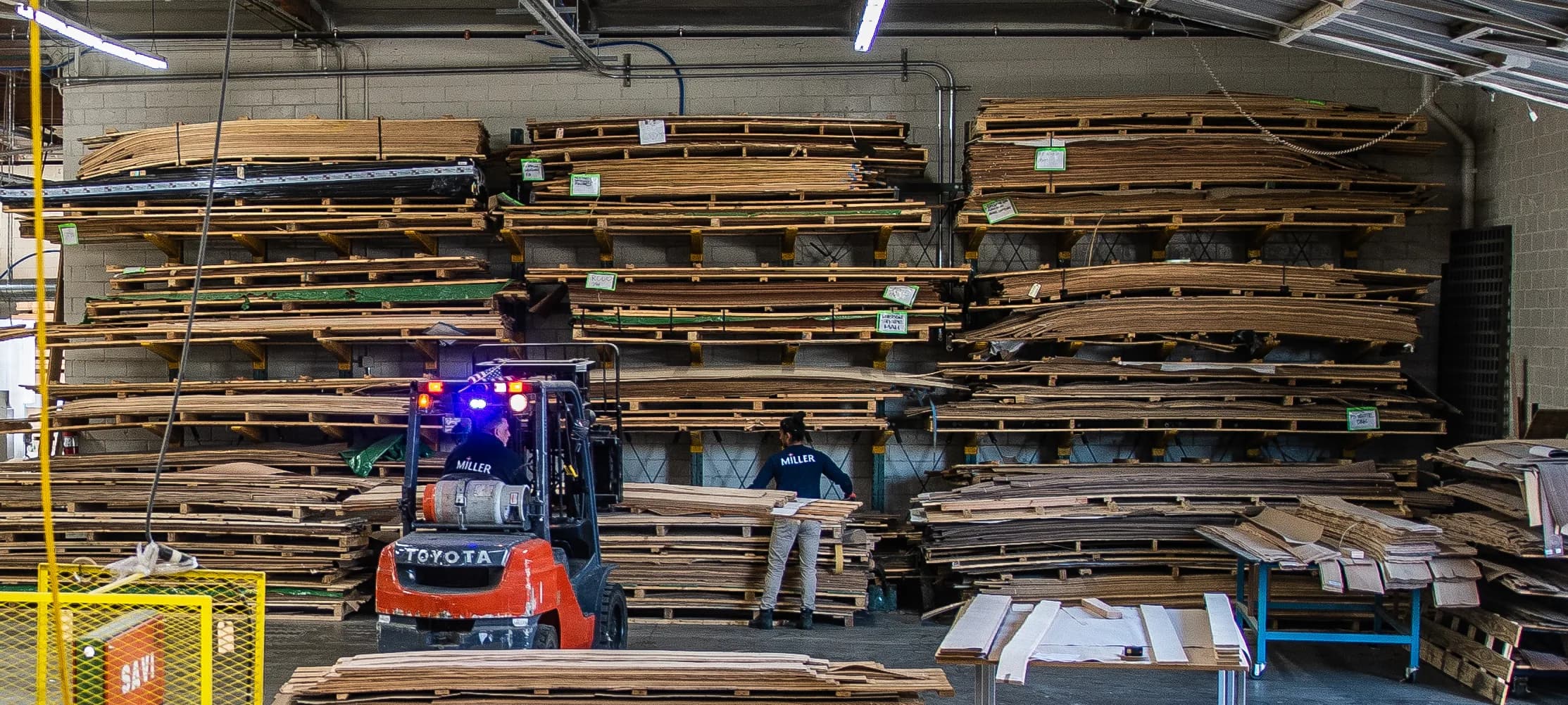 The veneer storage wall: flitches racked to the ceiling, each bundle tagged, a forklift and a shop hand pulling one down.